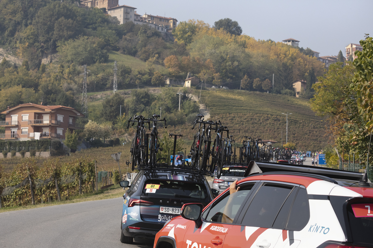 Gran Piemonte 2025 - The race convoy rounds a corner with trees beginning to show their autumnal colours in the distance