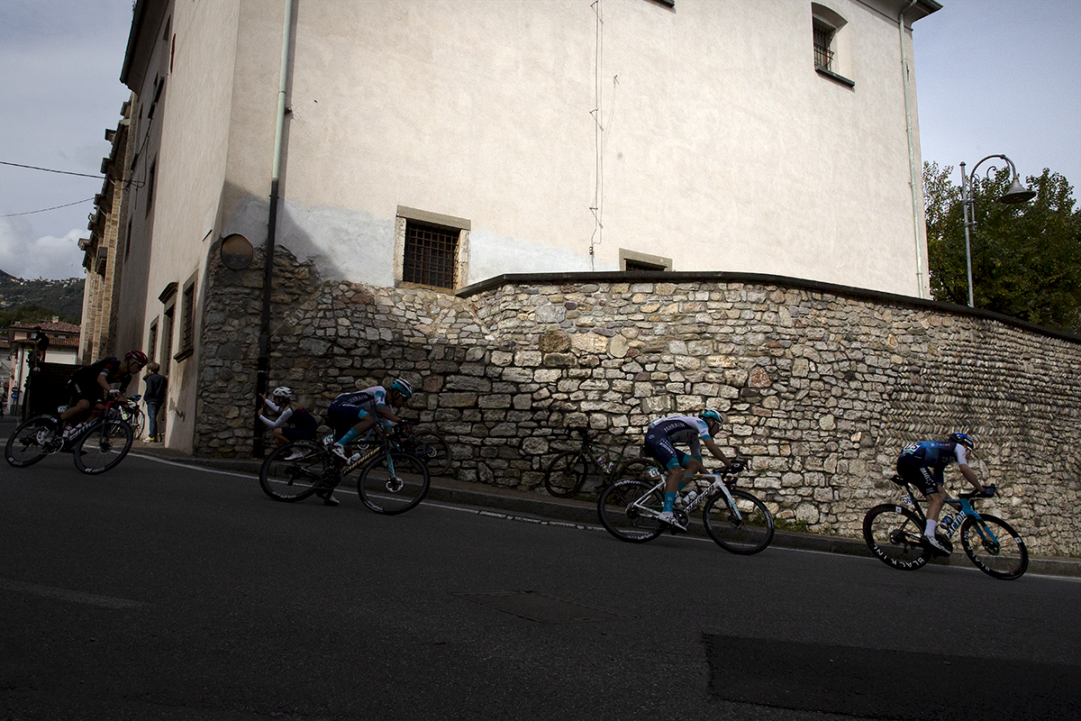 Il Lombardia 2024 - Riders take a corner past an old stone wall in Almenno San Salvatore