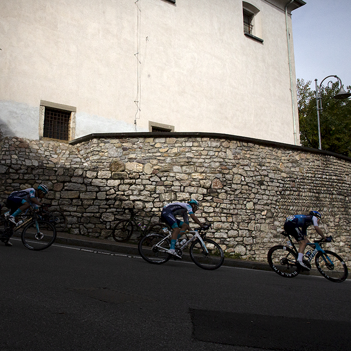 Il Lombardia 2024 - Riders take a corner past an old stone wall in Almenno San Salvatore