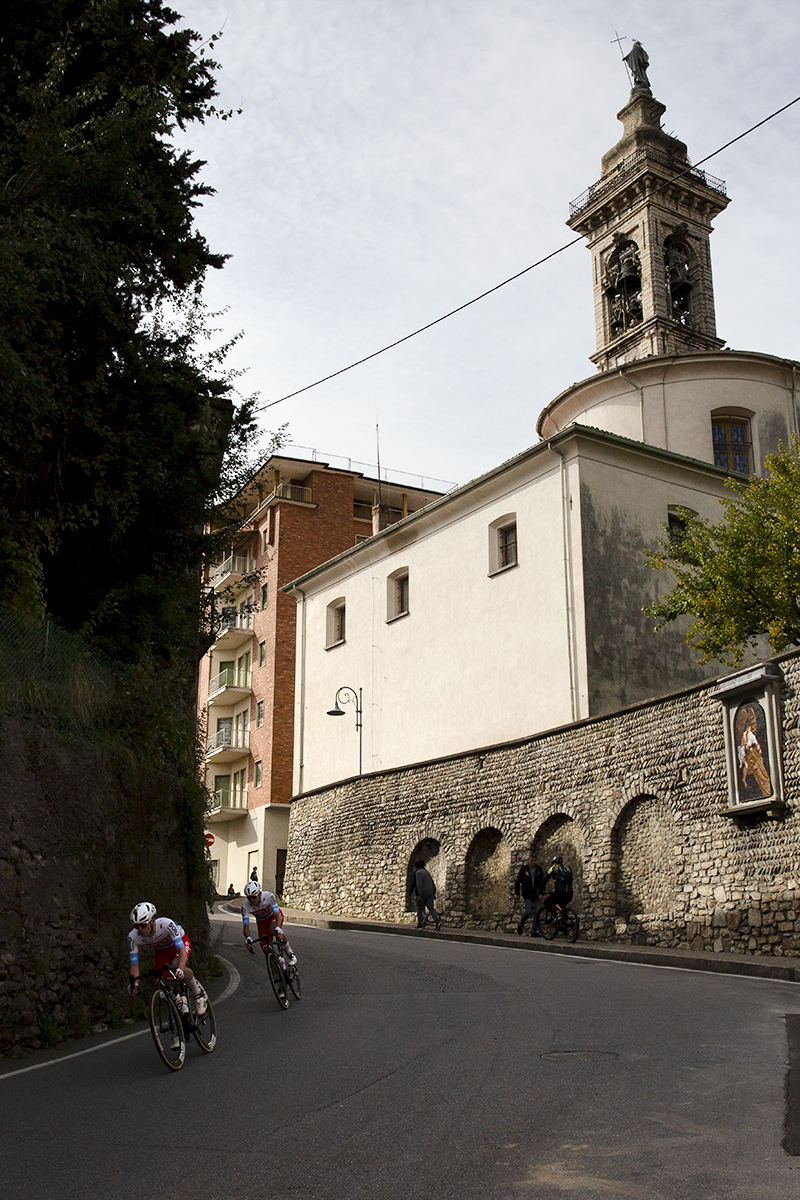 Il Lombardia 2024 - Two riders from [polti kometa] descend with the Chiesa Parrocchiale di San Salvatore Nuovo in the background