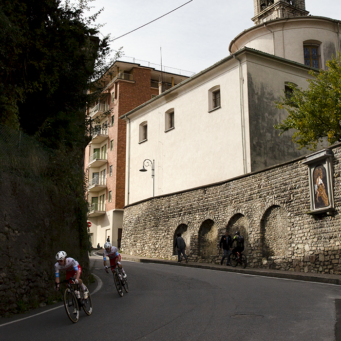 Il Lombardia 2024 - Two riders from [polti kometa] descend with the Chiesa Parrocchiale di San Salvatore Nuovo in the background