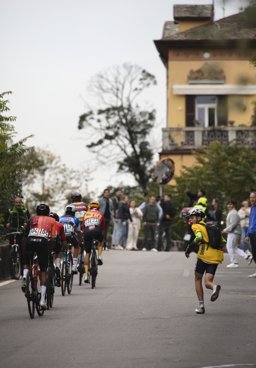 Il Lombardia 2024 - A young fan shouts support as he runs alongside a group of riders in Como