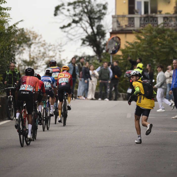 Il Lombardia 2024 - A young fan shouts support as he runs alongside a group of riders in Como