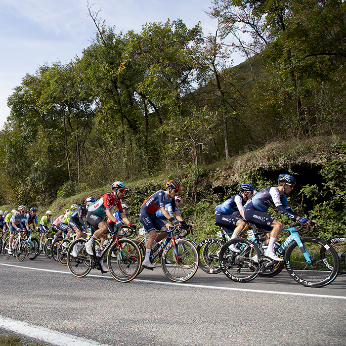 Il Lombardia 2024 - Riders climb past caves with hills in the background in Dosso