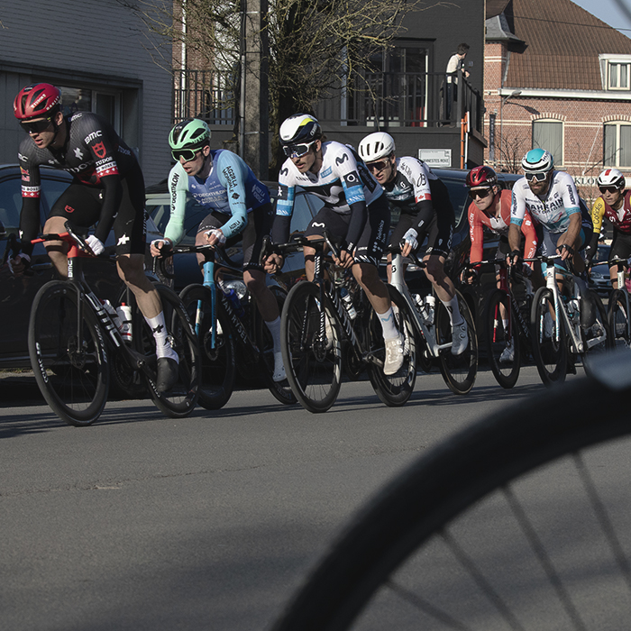 Kuurne Brussel Kuurne 2025 - The peloton races down the street seen through a bike parked in the foreground