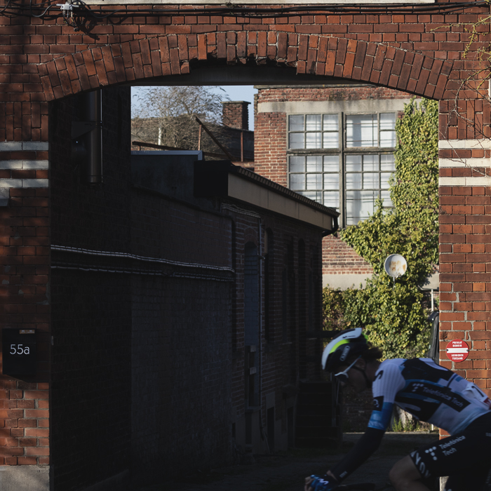 Kuurne Brussel Kuurne 2025 - A rider with his head bowed cycles in front of a brick arch with a statue of Jesus adorning it