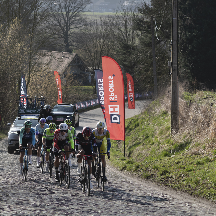 Kuurne Brussel Kuurne 2025 - A group of riders climbs the cobbles of Mont St-Laurent with the countryside in the background