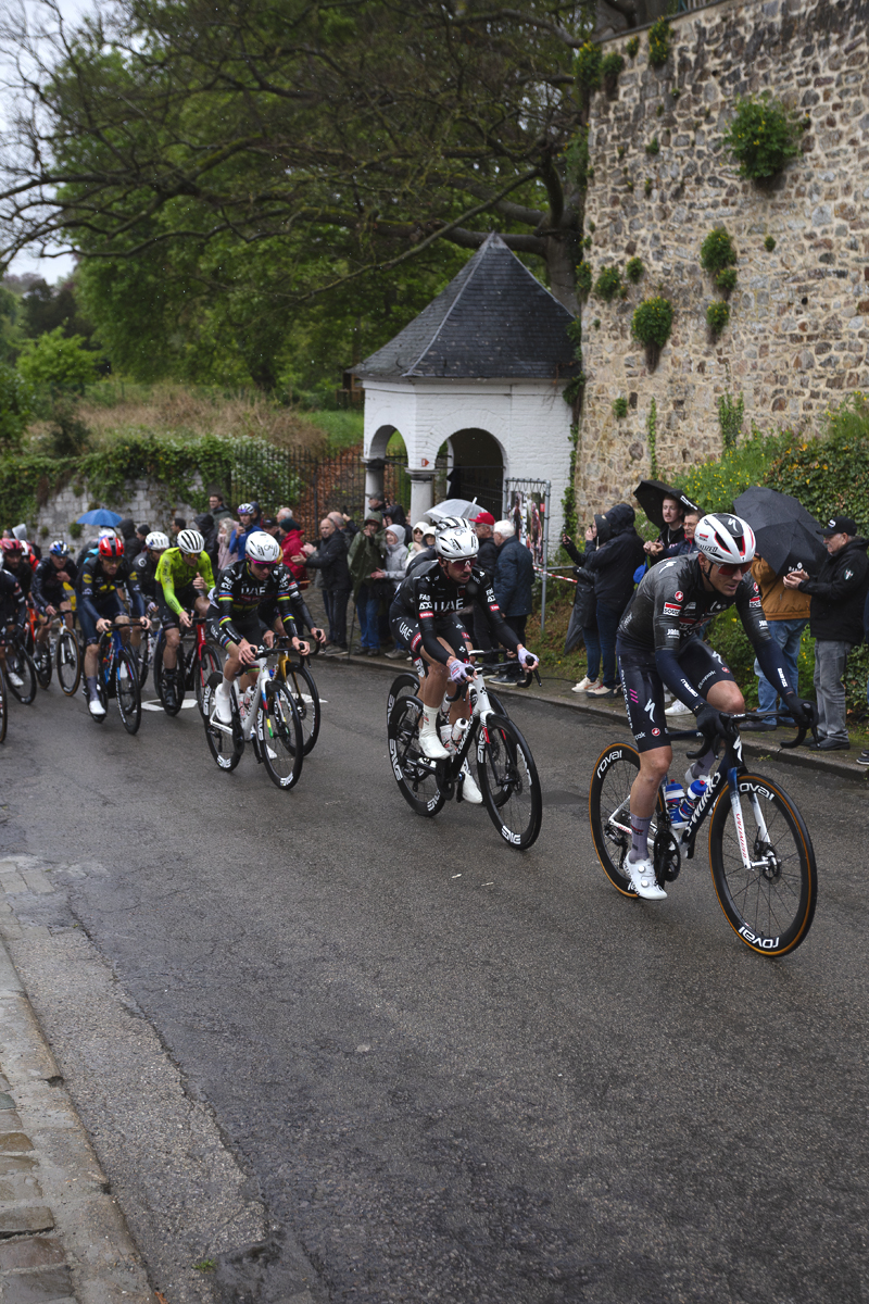 La Flèche Wallonne 2025 - A group of riders make their way past one of the small white chapels on Mur de Huy
