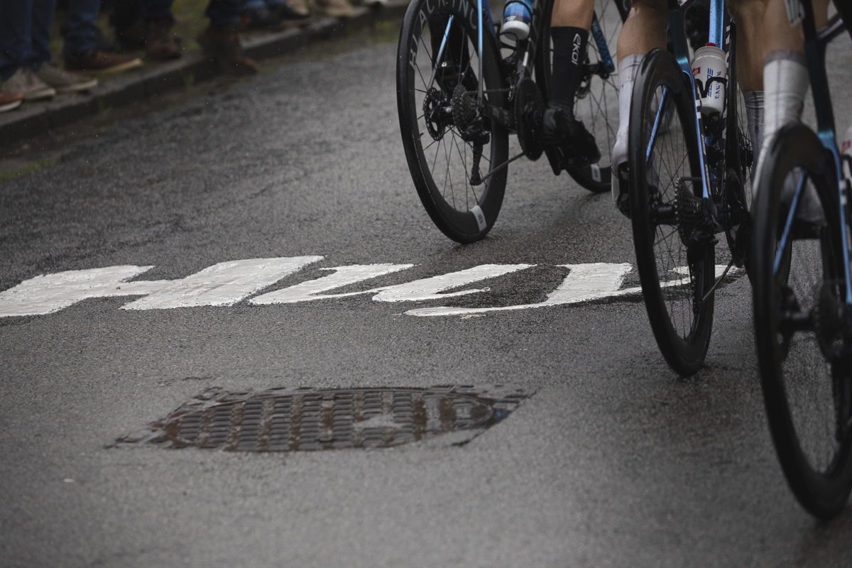 La Flèche Wallonne 2025 - Riders wheels are seen next to the word Huy written on the road on the Mur de Huy