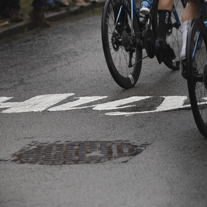 La Flèche Wallonne 2025 - Riders wheels are seen next to the word Huy written on the road on the Mur de Huy