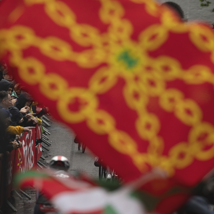 La Flèche Wallonne 2025 - Riders seen through flags being waved on the Mur de Huy