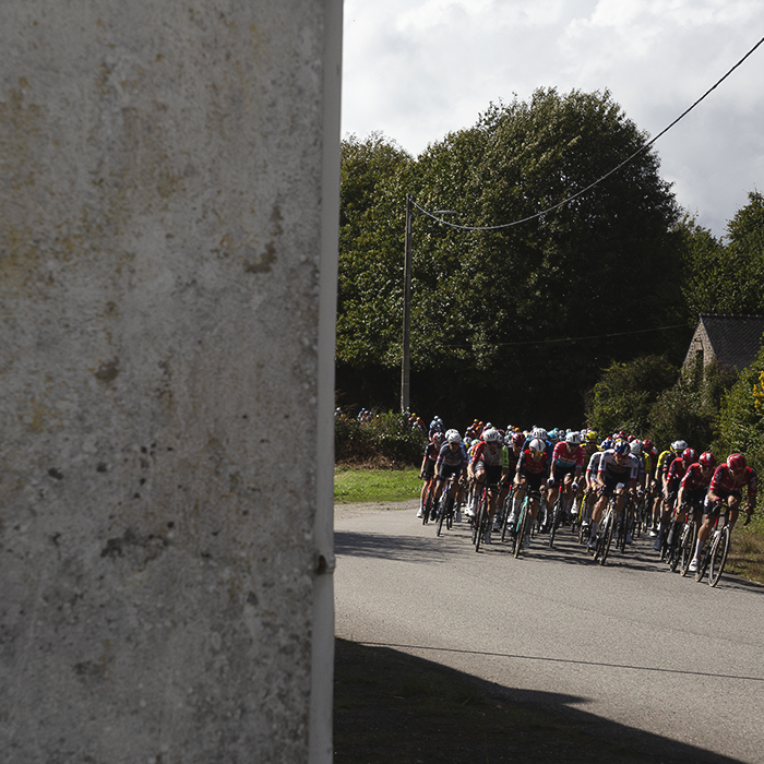 Bretagne Classic - Ouest-France 2025 - Riders are framed by the side of a house as they pass through Kersamuel