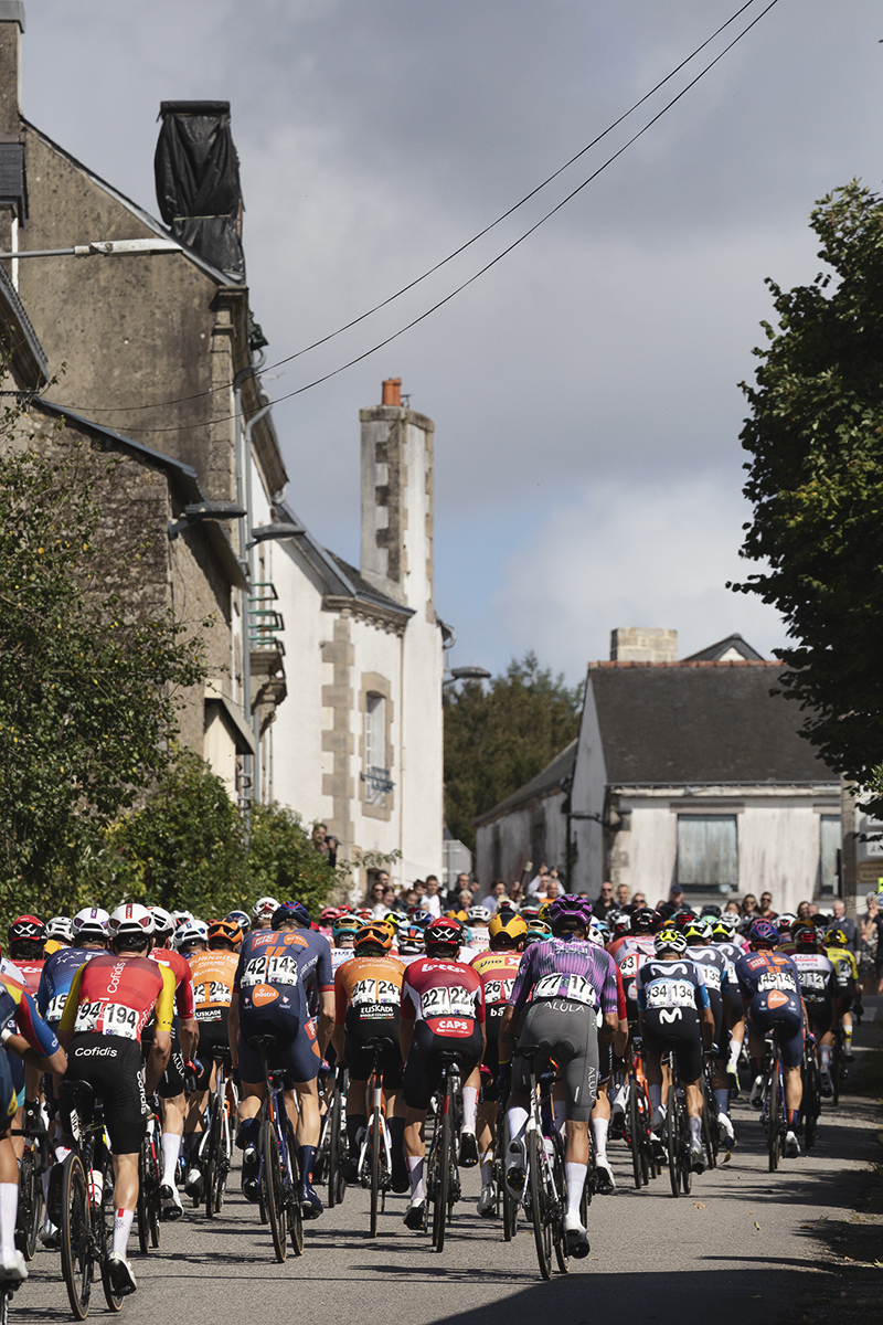 Bretagne Classic - Ouest-France 2025 - A rear view of the peloton as it passes up a street framed by traditional houses