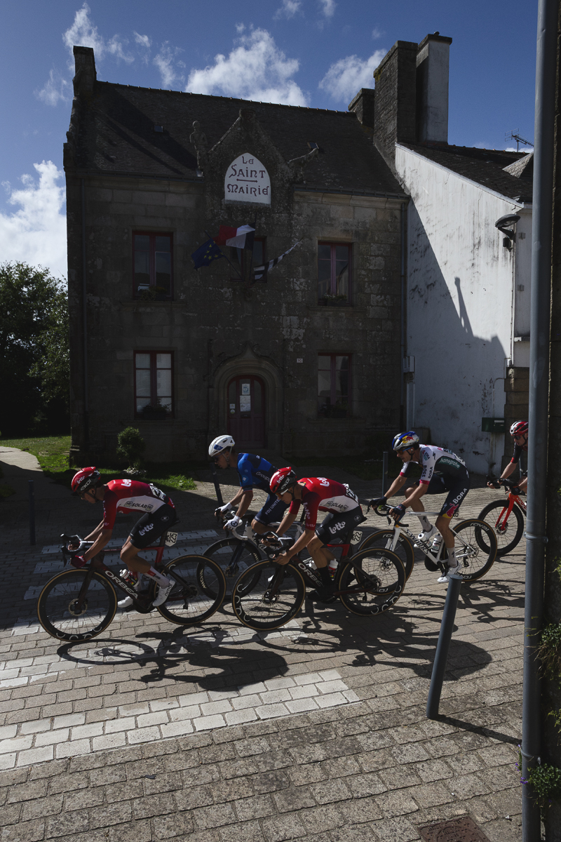 Bretagne Classic - Ouest-France 2025 - Riders pass in front of a traditional building flying the French flag in Le Saint