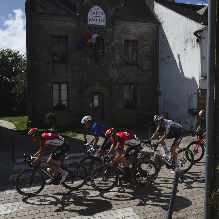 Bretagne Classic - Ouest-France 2025 - Riders pass in front of a traditional building flying the French flag in Le Saint