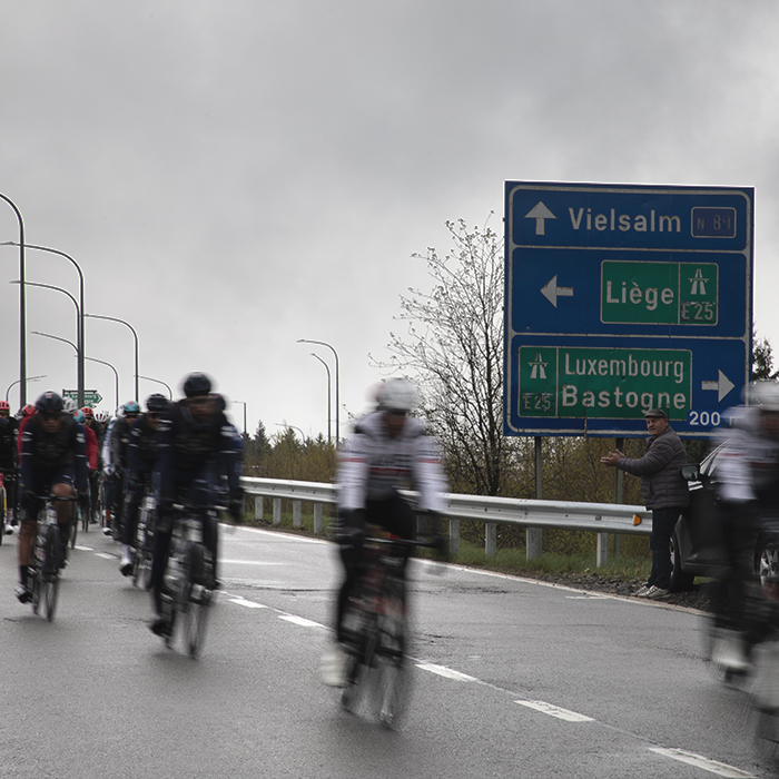 Liège-Bastogne-Liège 2024 - Riders speed past a sign pointing to Liege and Bastogne at Baraque Fraiture