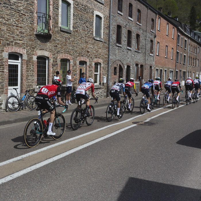 Liege Bastogne Liege 2025 - Riders pass tall stone houses at La Roché-en-Ardenne