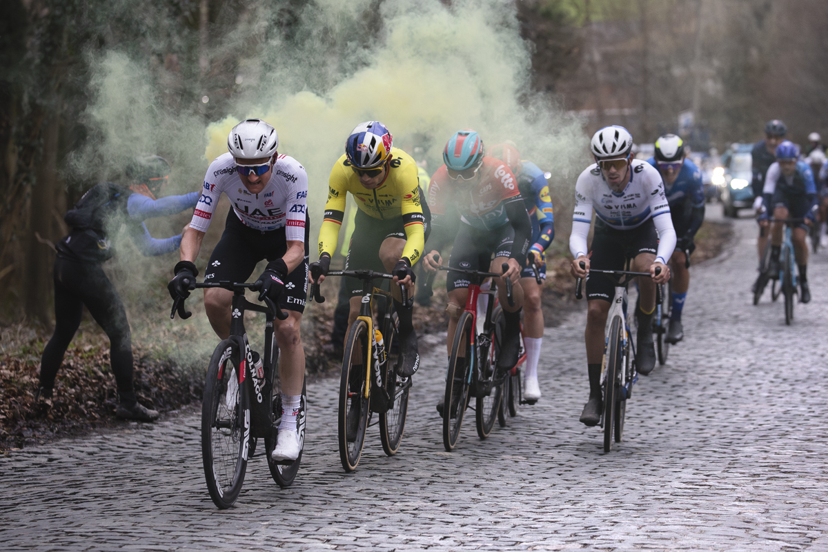 Omloop Het Nieuwsblad 2024 - Riders pass a fan with a yellow flare on Bosberg