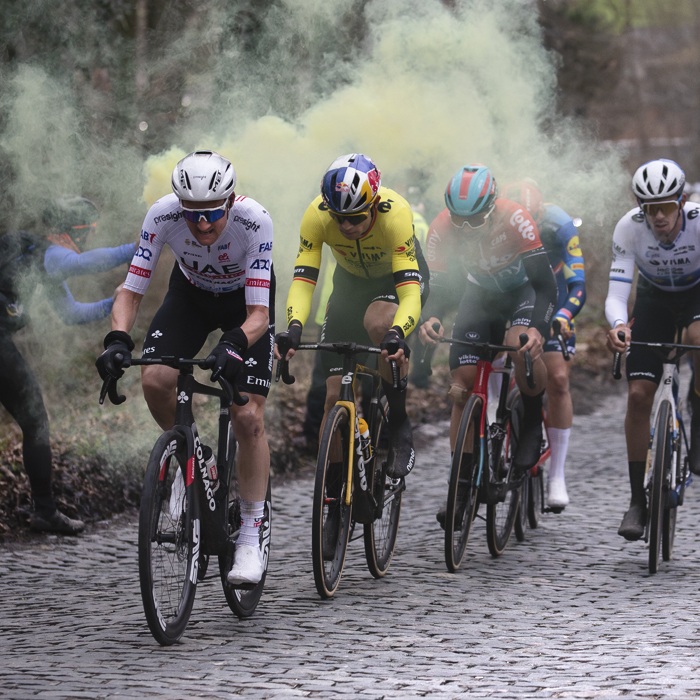 Omloop Het Nieuwsblad 2024 - Riders pass a fan with a yellow flare on Bosberg