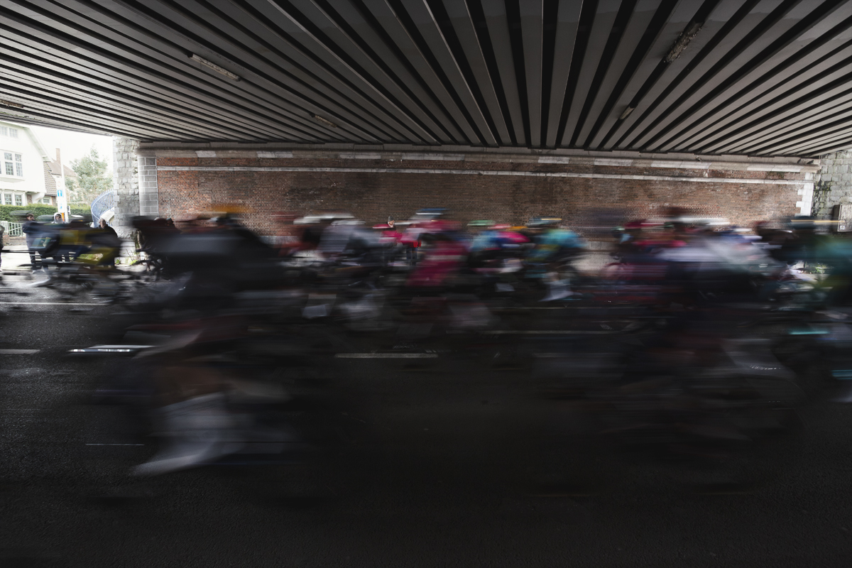 Omloop Nieuwsblad 2025 - Riders speed under a bridge in Gent