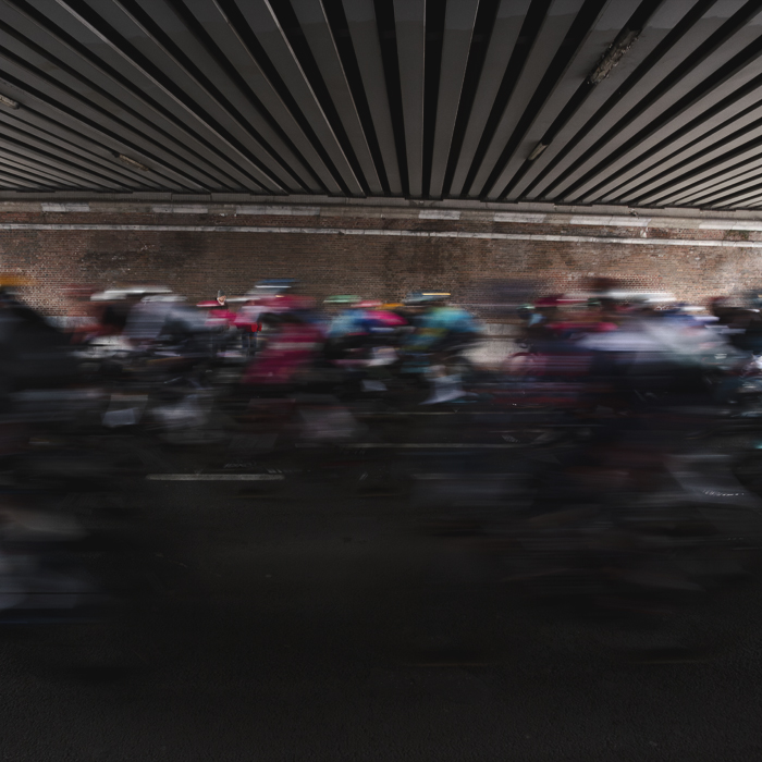 Omloop Nieuwsblad 2025 - Riders speed under a bridge in Gent