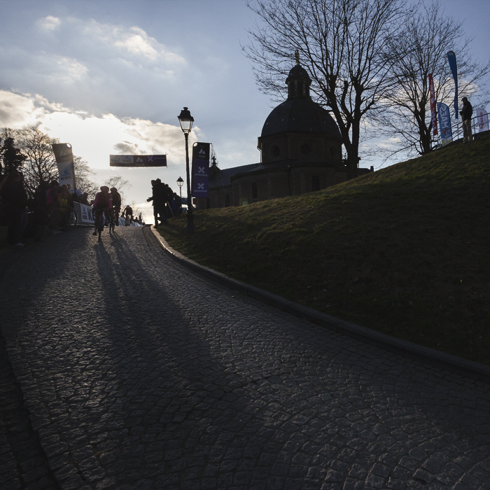 Omloop Nieuwsblad Vrouwen 2025 - Riders crest the Muur van Geraardsbergen silhouetted in the winter sun