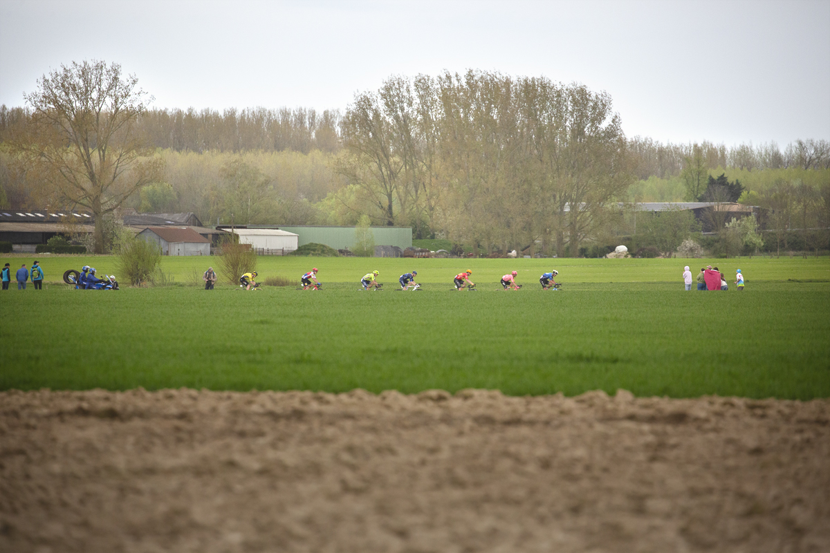 Paris Roubaix 2024 - A group of riders viewed across the fields on Camphin-en-Pévèle