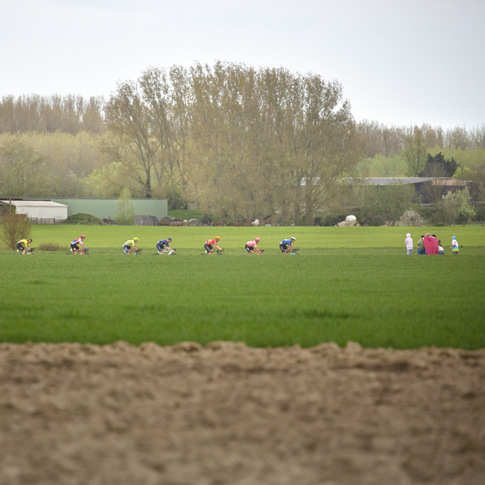 Paris Roubaix 2024 - A group of riders viewed across the fields on Camphin-en-Pévèle
