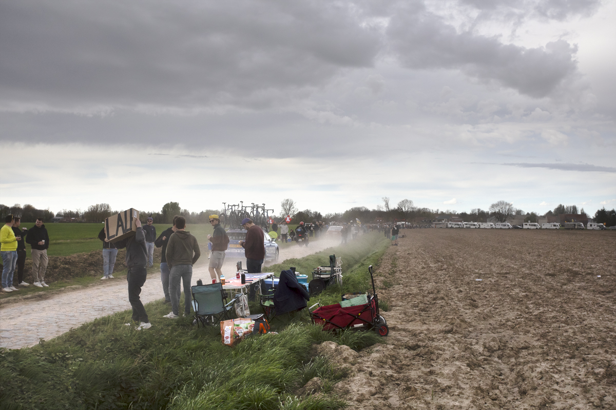Paris Roubaix 2024 - Fans line the sides of Camphin-en-Pévèle as passing cars kick up dust