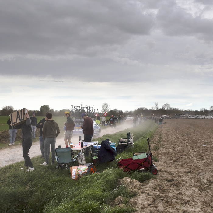 Paris Roubaix 2024 - Fans line the sides of Camphin-en-Pévèle as passing cars kick up dust