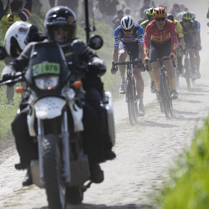 Paris Roubaix 2024 - Dust is kicked up by a motorbike in front of riders on the Quiévy à Saint-Python sector