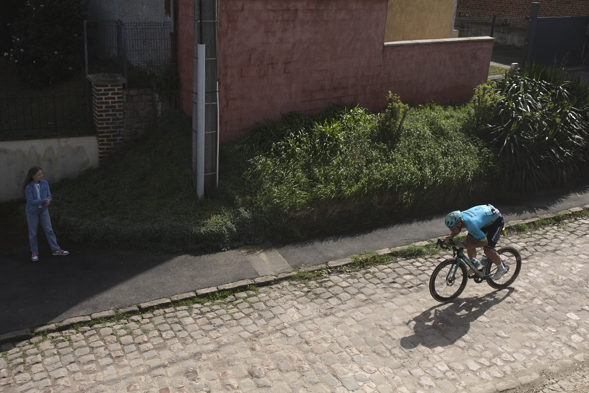 Paris Roubaix 2024 - Gleb Syritsa of Astana Qazaqstan Team seen from above passes a young girl at the start of the Quiévy à Saint-Python sector