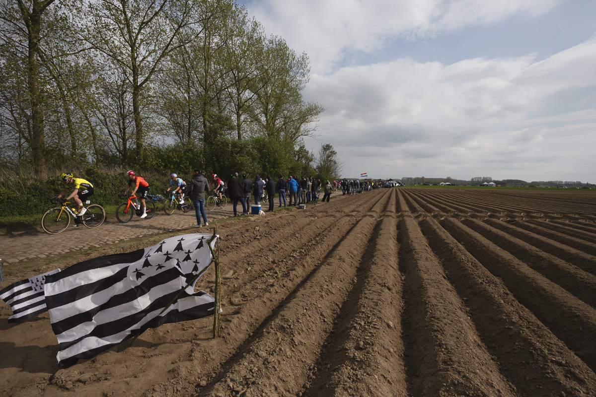 Paris Roubaix 2025 - A flag of Brittany planted in the furrows of a ploughed field as the riders pass by
