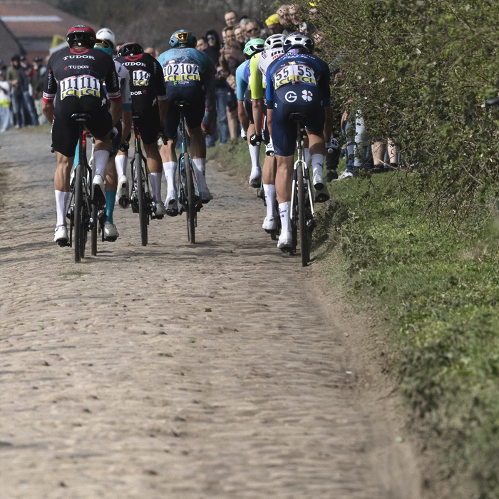 Paris Roubaix 2025 - A group of riders from behind with the cobbles of Camphin-En-Pévèle in the foreground