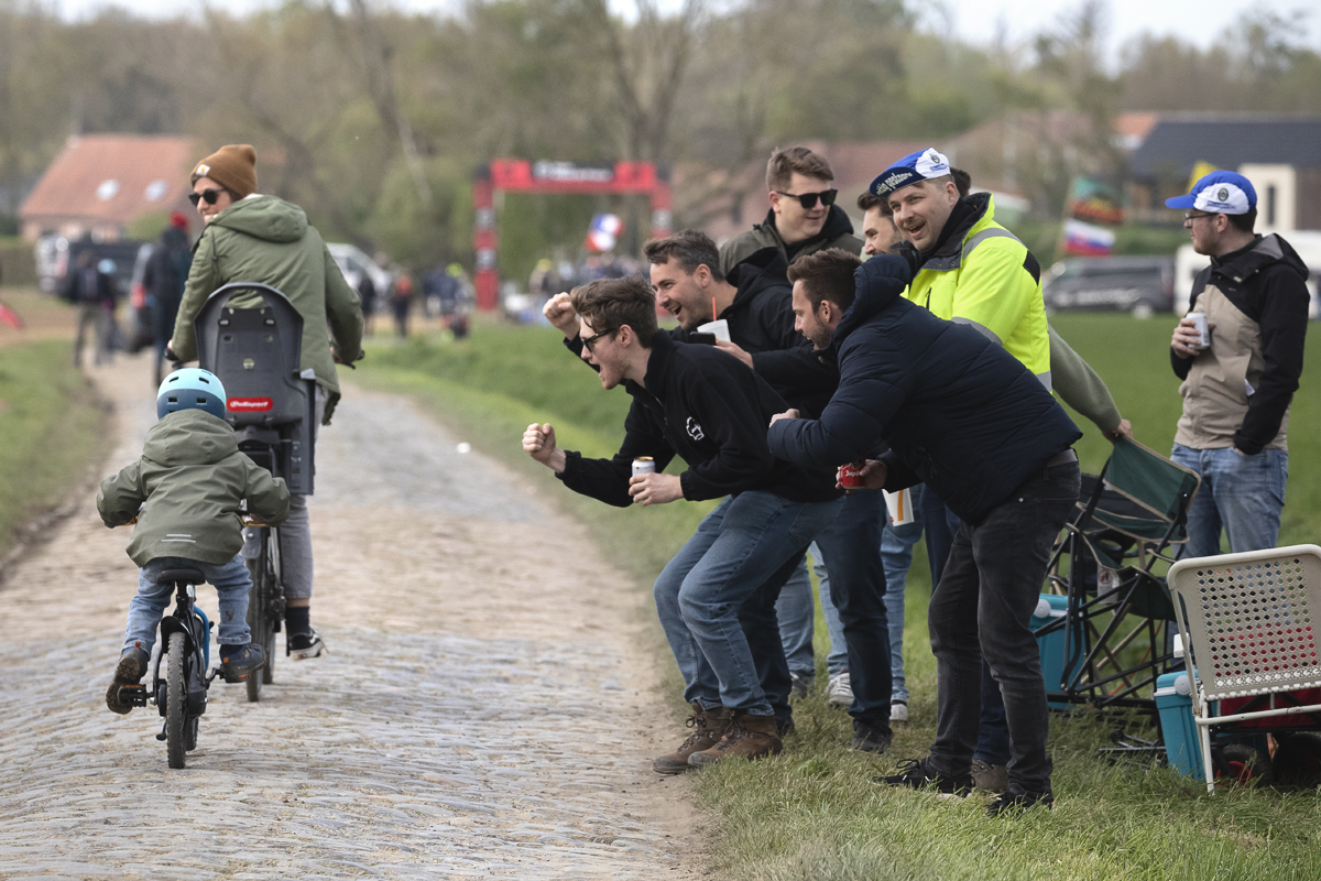 Paris Roubaix 2025 - A young fan and their mother are cheered on by a group of fans as they ride on the cobbles