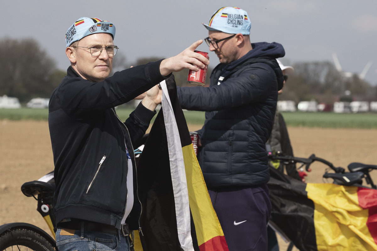 Paris Roubaix 2025 - A Belgian fan points into the distance, flag in one hand, can of local beer in the other