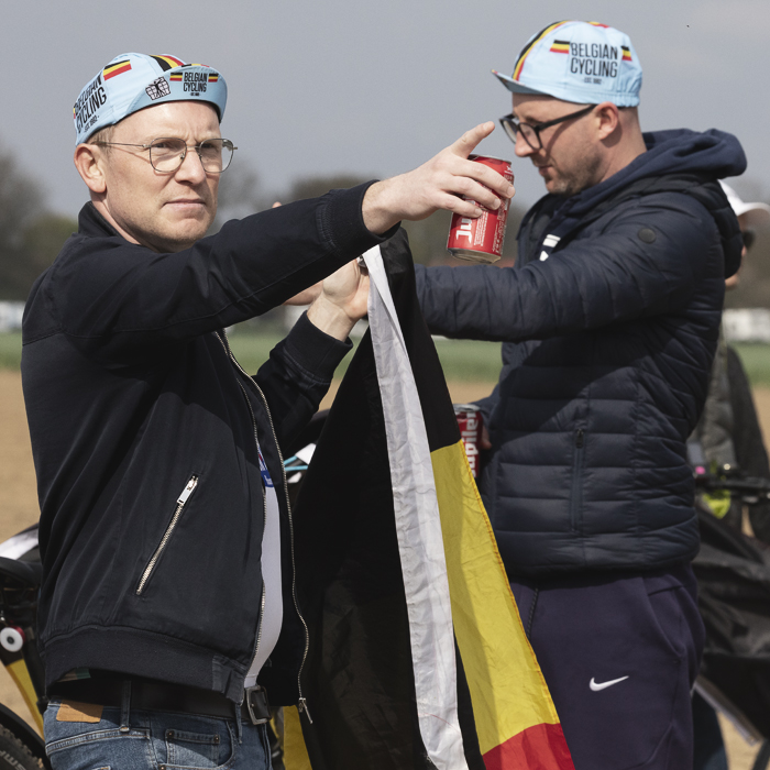 Paris Roubaix 2025 - A Belgian fan points into the distance, flag in one hand, can of local beer in the other