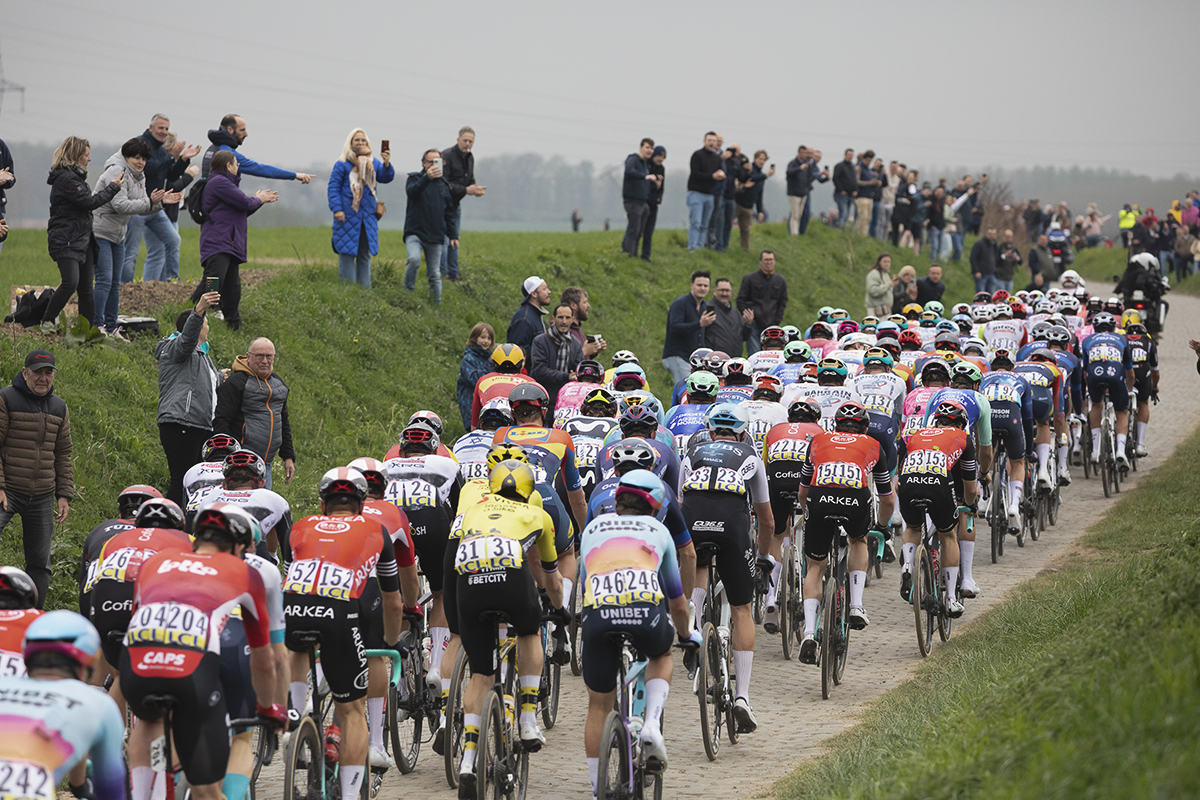 Paris Roubaix 2025 - A rear view of the peloton with fans lining the banks at either side of the road