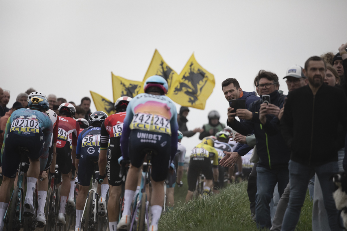 Paris Roubaix 2025 - A rear view riders with the flags of Flanders flying on Quérénaing à Maing