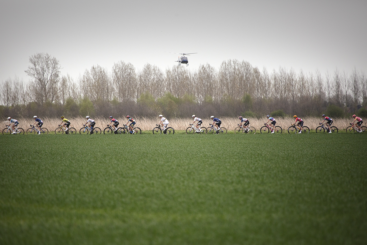 Paris Roubaix Femmes 2024 - A strung out group of riders are filmed by a helicopter on the Bourghelles à Wannehain sector