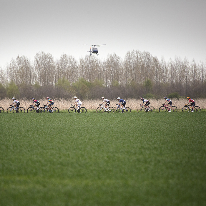 Paris Roubaix Femmes 2024 - A strung out group of riders are filmed by a helicopter on the Bourghelles à Wannehain sector