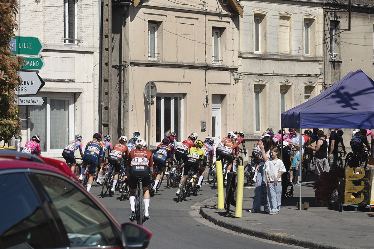 Paris Roubaix Femmes 2025 - Riders round a corner watched by young spectators at the start of the race