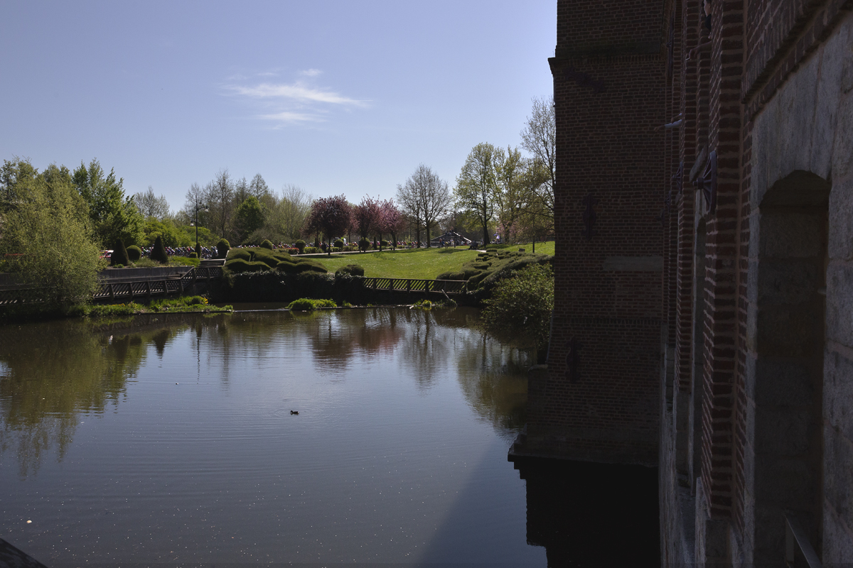 Paris Roubaix Femmes 2025 - Riders viewed from across a large landscaped mill pond in Denain