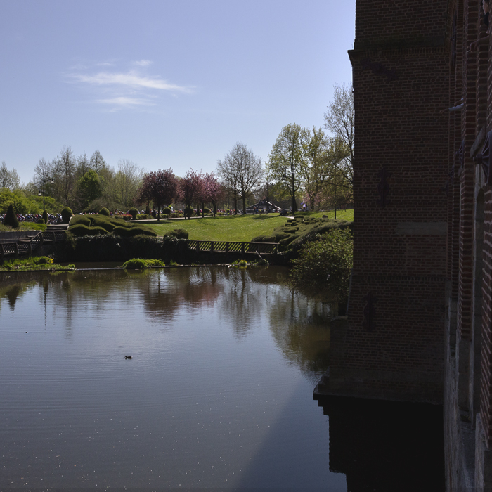 Paris Roubaix Femmes 2025 - Riders viewed from across a large landscaped mill pond in Denain