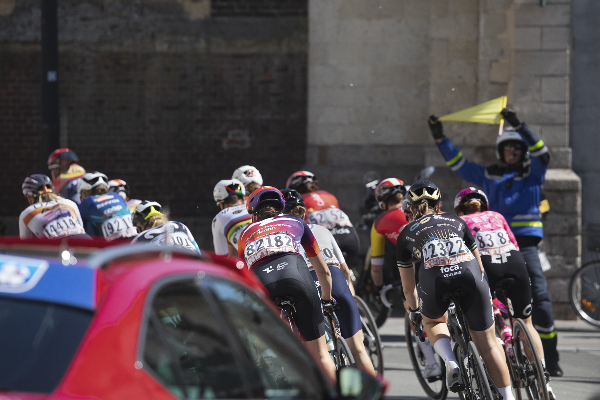 Paris Roubaix Femmes 2025 - A flag bearer warns riders of a corner in front of the Paroisse Saint Martin de Denain