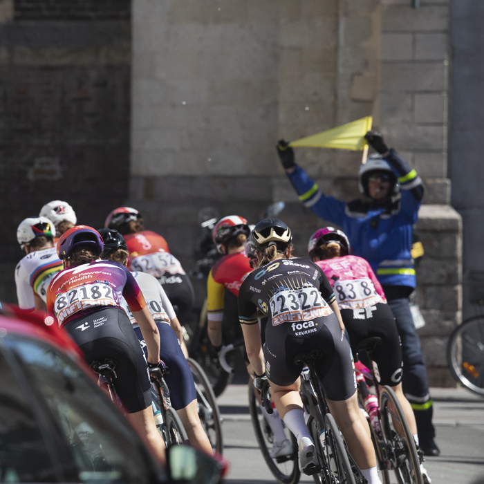Paris Roubaix Femmes 2025 - A flag bearer warns riders of a corner in front of the Paroisse Saint Martin de Denain