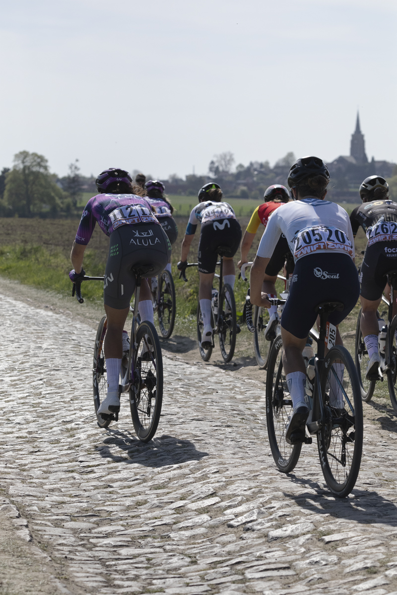 Paris Roubaix Femmes 2025 - A group of riders on Mons-en-Pévèle with a church spire in the distance