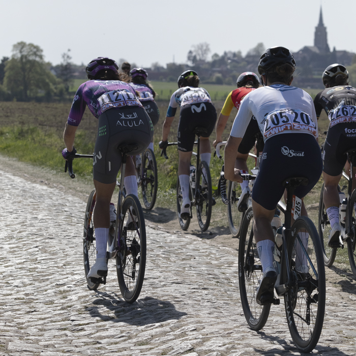 Paris Roubaix Femmes 2025 - A group of riders on Mons-en-Pévèle with a church spire in the distance