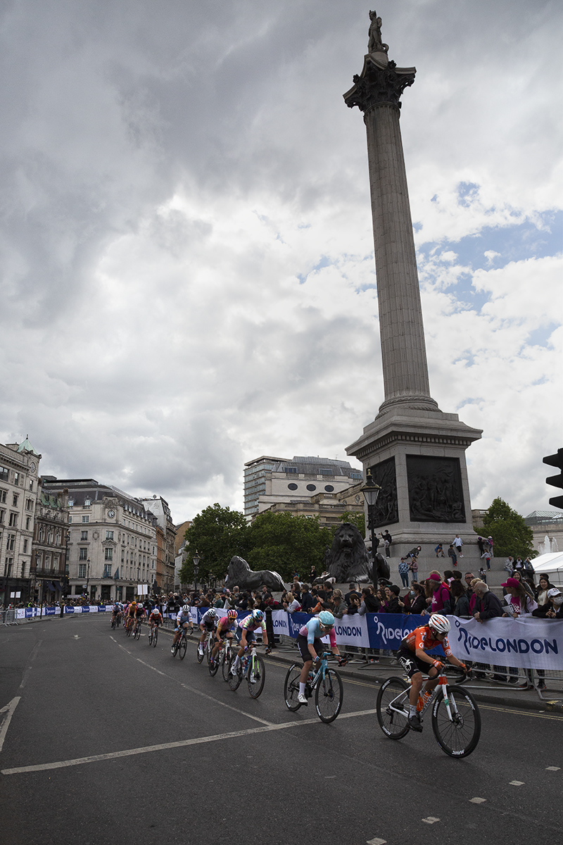 RideLondon Classique 2022 - A strung out group of riders speed through Trafalgar Square past Nelson’s Column