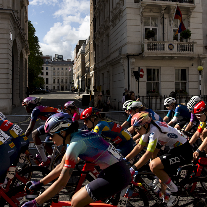 RideLondon Classique 2024 - The peloton on Pall Mall with grand stone buildings behind them